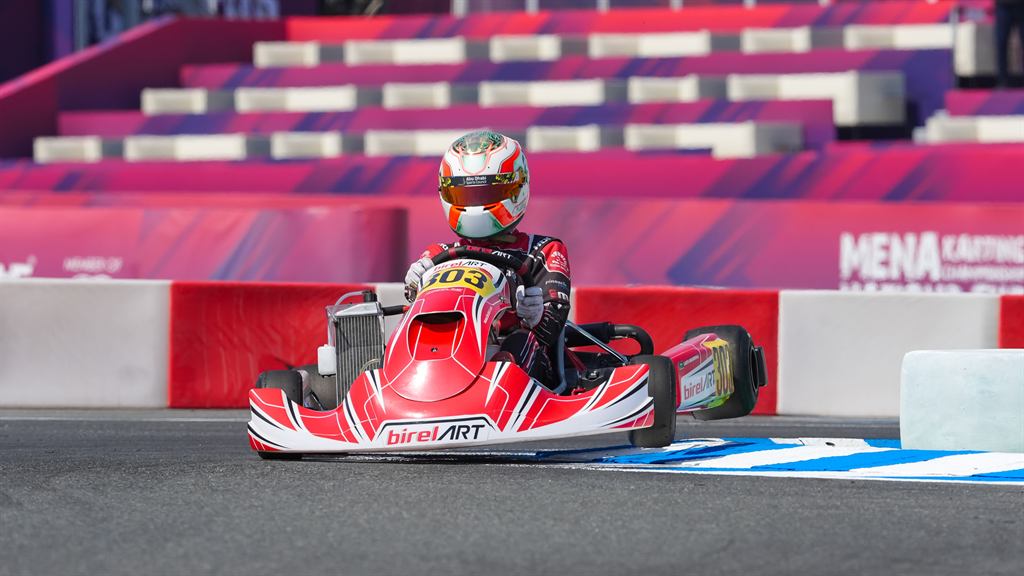 Kart on track approaching a corner, pit boards in the background